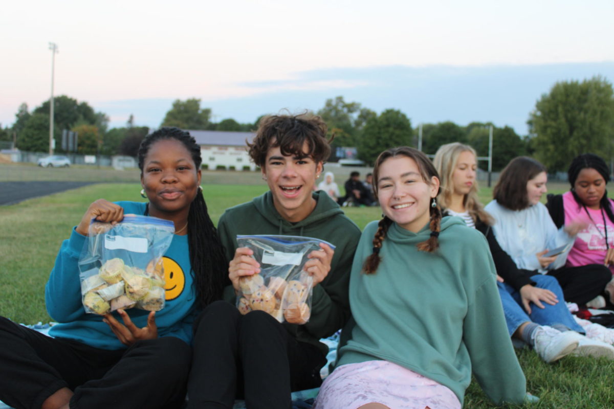 Seniors Ruth Dunn, Griffin Caughron, and Scarlett Bertram posing with baked muffins at senior sunrise on September 15th, 2023.
