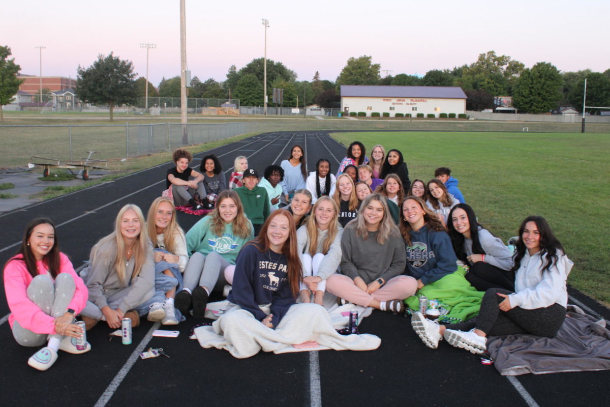 Part of the senior class wrapped up in blankets posing for the picture on the track field, as the sun comes up for senior sunrise.