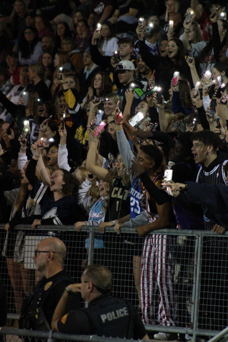 Members of the student section hold up flashlights and cheer on the football team. 