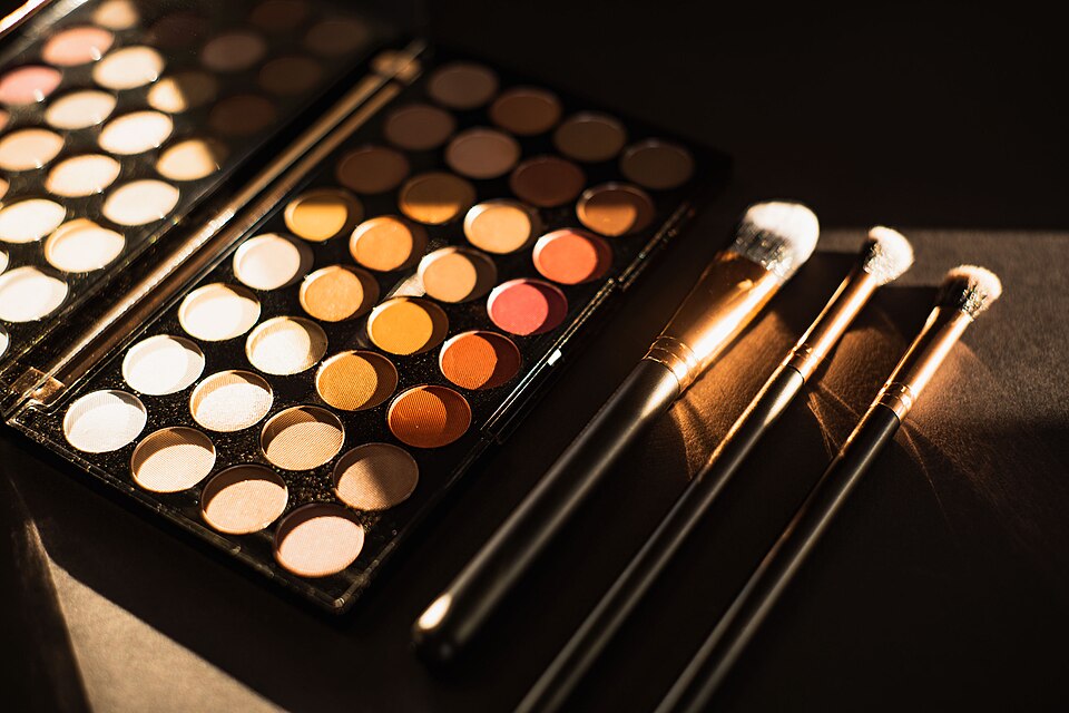 Eyeshadow sits alongside three makeup brushes under the sunlight. 