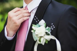 A teen boy adjusts his tie while he looks out into the distance. Many teenagers attend prom each year and it is looked forward to by many.