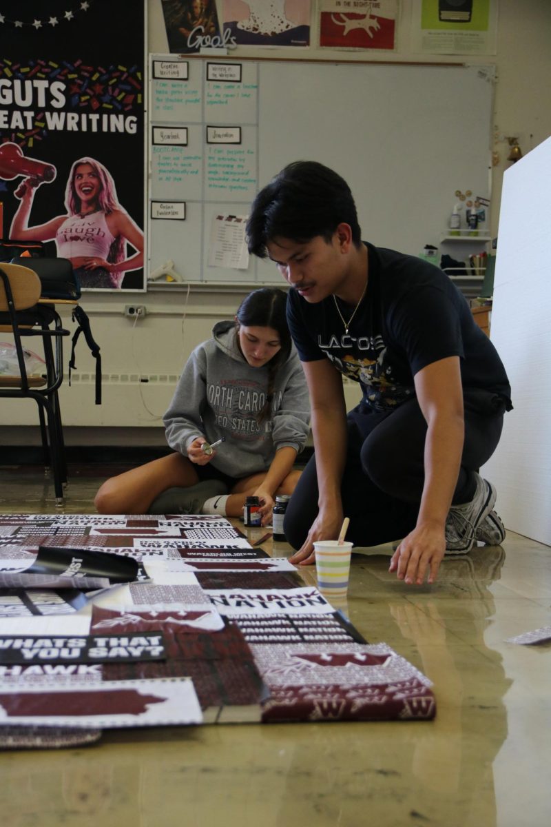 Seniors Alyssa Muheljic and Jay Esmael glue down printed logos designed by Esmael onto the backdrop. 