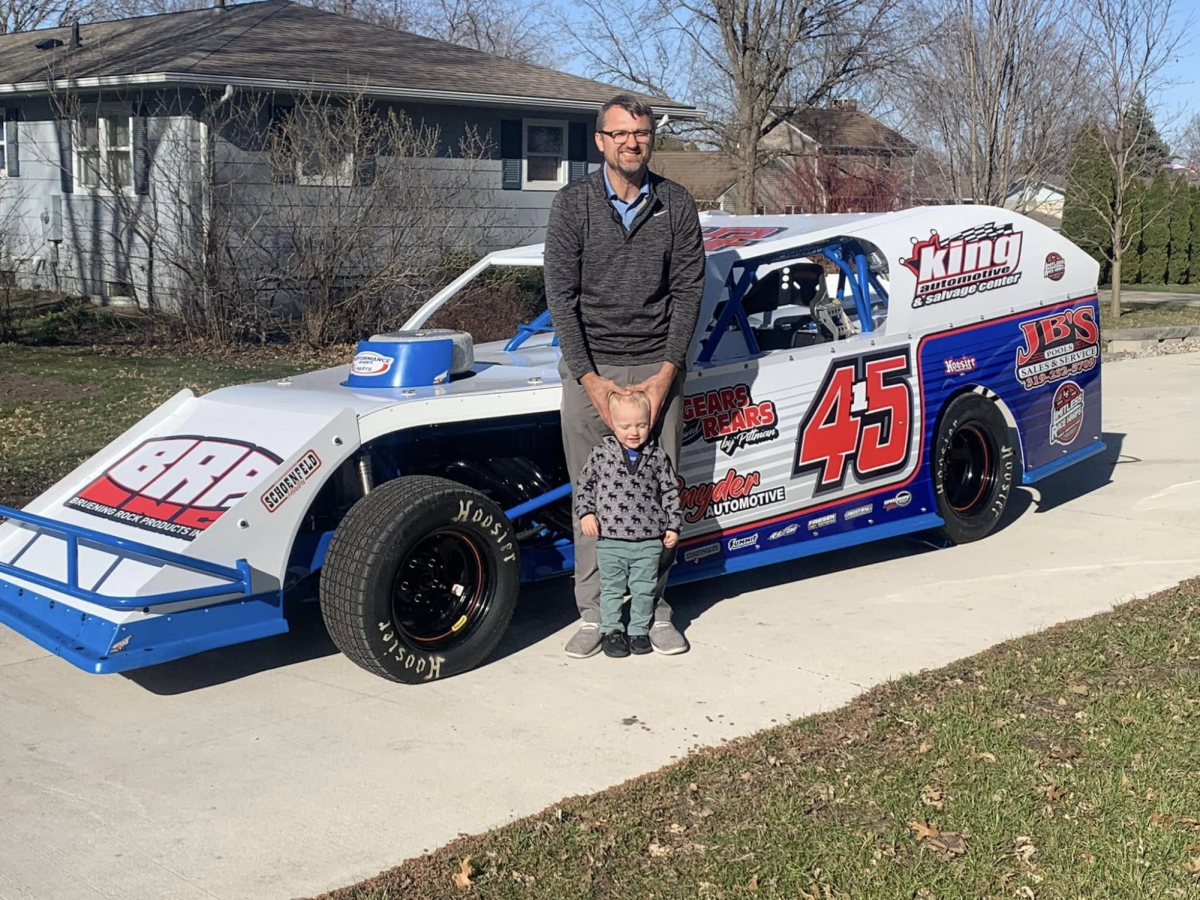 A photo of Barta and his son standing in front of his race car.